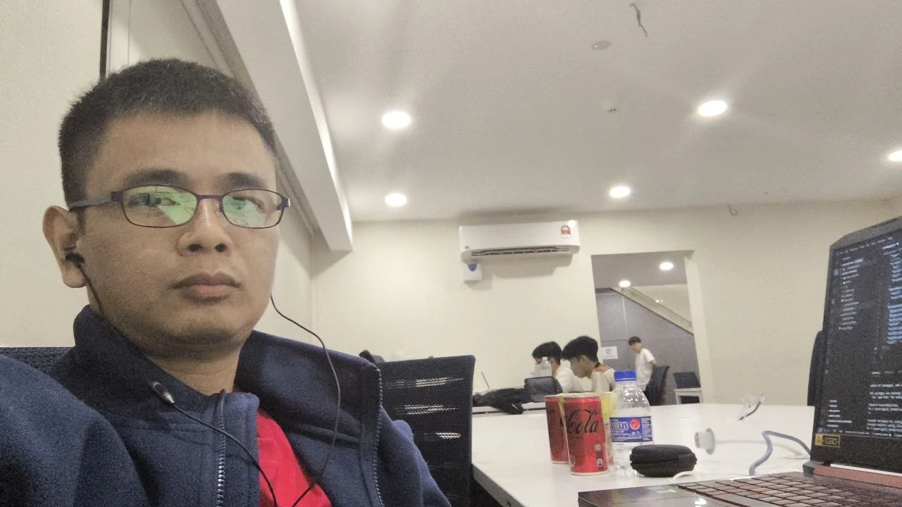 Focused coding session in a shared workspace with laptop and teammates in the background